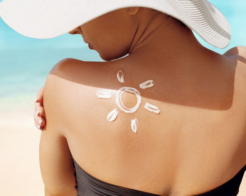 Frau am Strand mit sonnenförmigem Sonnenschutzmittel auf der Schulter