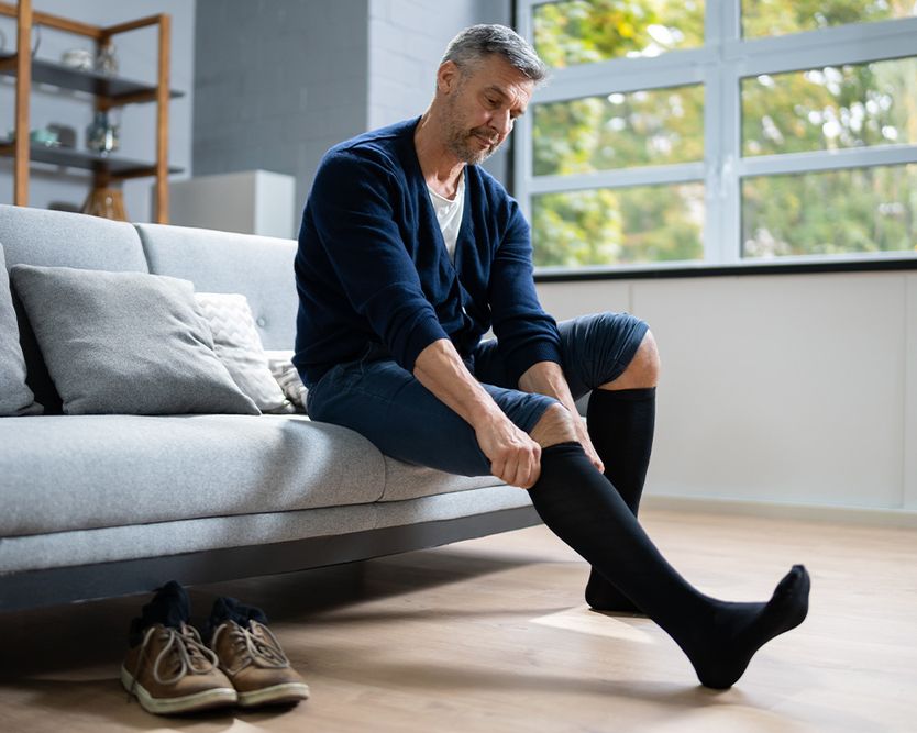 Eine Person, die auf einem grauen Sofa sitzt und schwarze Kompressionsstrümpfe anzieht